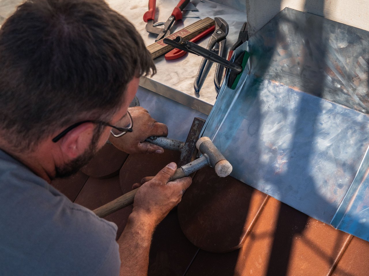 Flaschner passt ein Zinkblech mit dem Hammer am Dachanschluss an