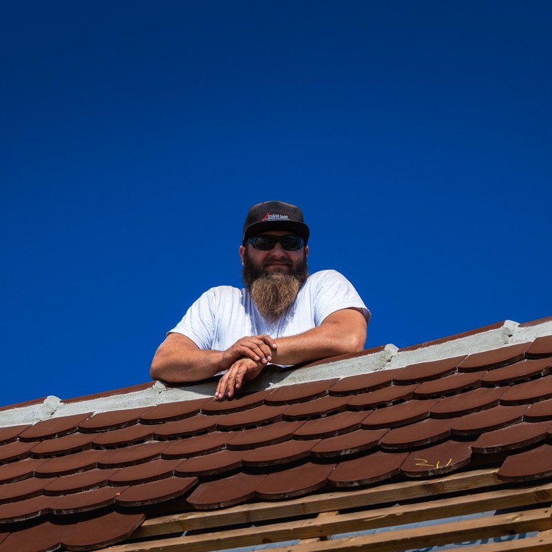 Zimmerer mit Vollbart und Sonnenbrille auf dem Dach